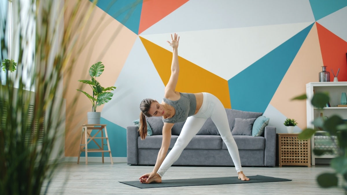 Portrait of cute lady in leggings and top doing yoga at home working out standing on mat exercising. Healthy youth lifestyle and indoor activities concept.